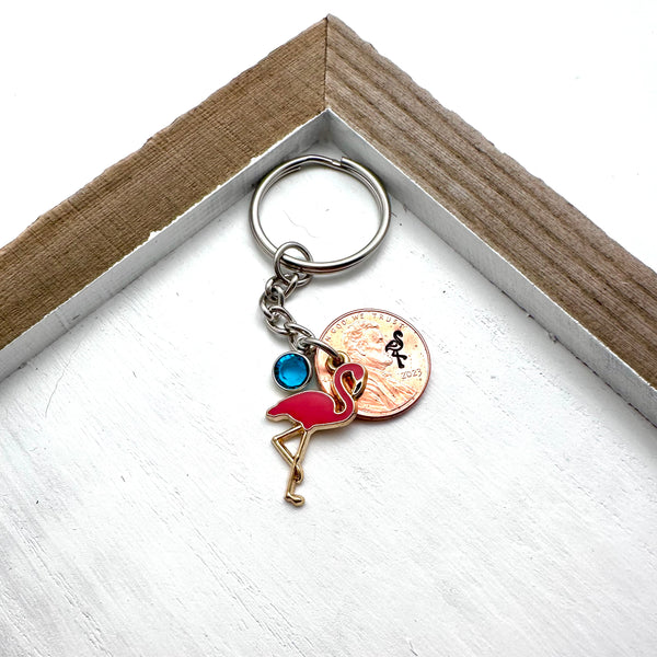 Pink flamingo charm on a keychain with birthstone and lucky penny with flamingo stamp.