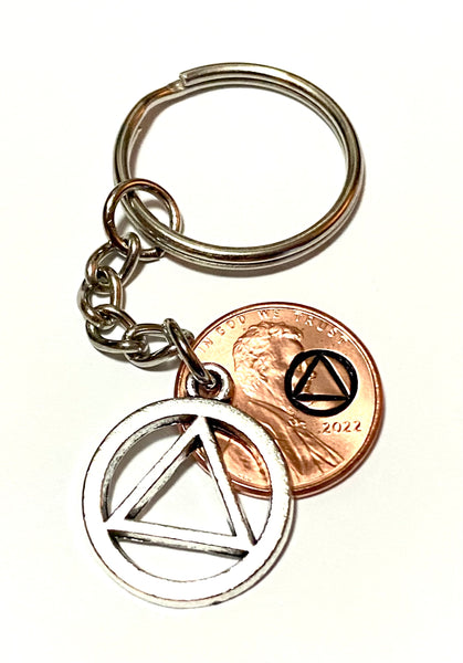 A Lucky Penny Keychain with a silver AA Alcoholics Anonymous Recovery Symbol attached to a Lincoln Cent engraved with the Sobriety symbol above the date.