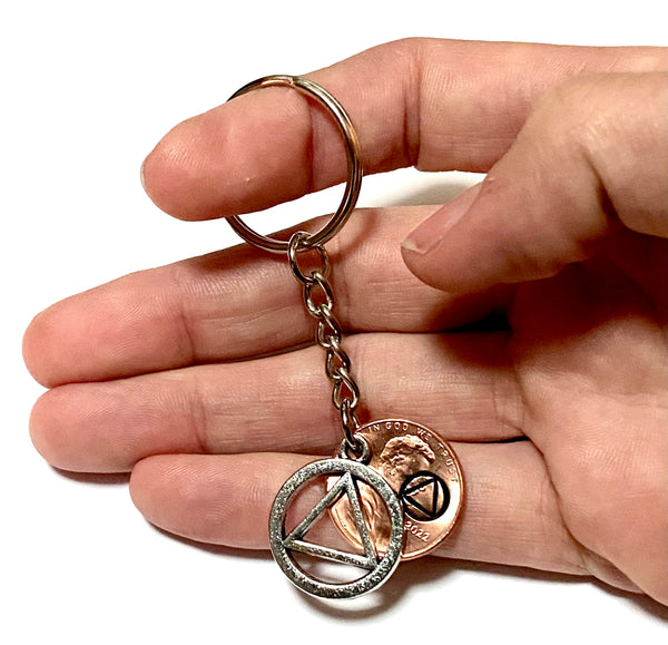 A Lucky Penny Keychain with a silver AA Alcoholics Anonymous Recovery Symbol attached to a Lincoln Cent engraved with the Sobriety symbol above the date.