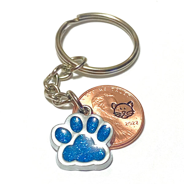 A light blue glitter charm of a cat's paw with a hand stamped penny with a cat's face on a lucky penny keychain.