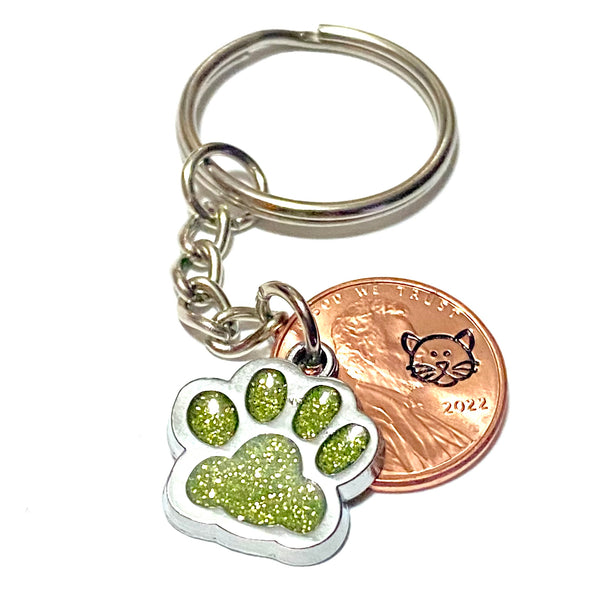 A yellow glitter charm of a cat's paw with a hand stamped penny with a cat's face on a lucky penny keychain.