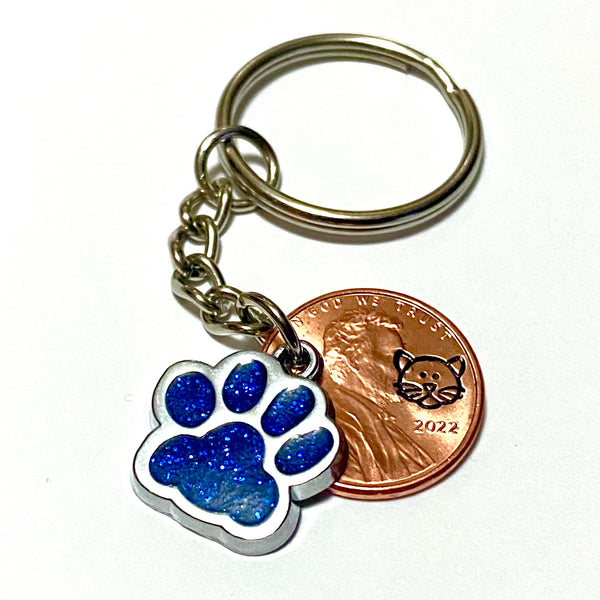 A blue glitter charm of a cat's paw with a hand stamped penny with a cat's face on a lucky penny keychain.