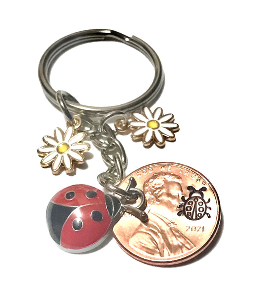 Ladybug and 2 white flower Charms with an engraved Ladybug above the date of a Lincoln Cent on this Lucky Penny Keychain.
