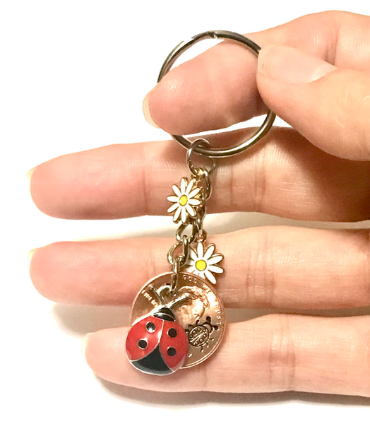 Ladybug and 2 white flower Charms with an engraved Ladybug above the date of a Lincoln Cent on this Lucky Penny Keychain.
