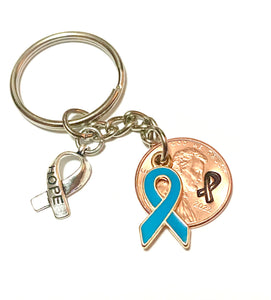 A blue awareness ribbon along with a silver HOPE charm attached to a Lincoln Cent that is hand stamped with a detailed ribbon design to make a great Lucky Penny Keychain.