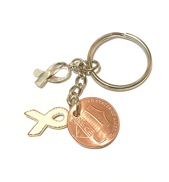 A blue awareness ribbon along with a silver HOPE charm attached to a Lincoln Cent that is hand stamped with a detailed ribbon design to make a great Lucky Penny Keychain.