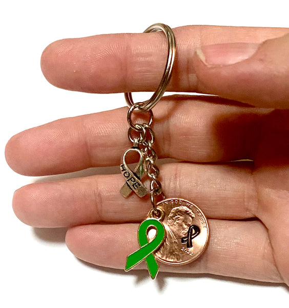 A green ribbon charm for mental health awareness month with a silver HOPE charm attached to a Lincoln Cent engraved with a detailed design of an awareness ribbon for a great Lucky Penny Keychain!