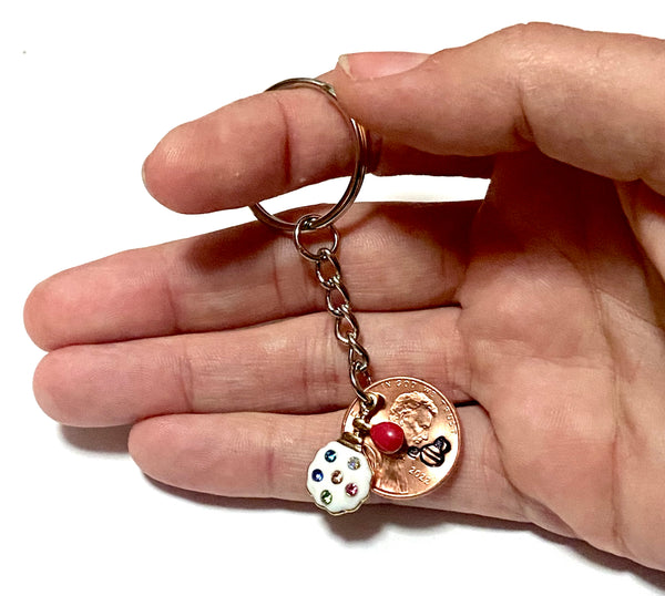 A Lucky Penny Keychain with a rhinestone charm of a vintage perfume bottle and atomizer attached to a Lincoln Cent with a perfume bottle silhouette above the date.
