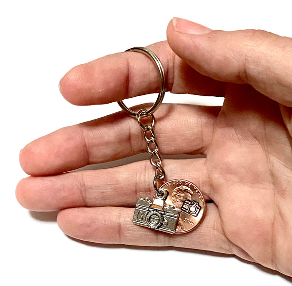 A photography inspired keychain with a silver camera charm attached to a Lincoln Cent with a camera design engraved above the date. It's an awesome Lucky Penny Keychain!