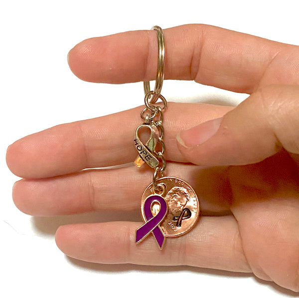 A purple awareness ribbon charm along with a silver HOPE charm attached to a Lincoln Cent with a detailed design of an awareness ribbon above the date for a great Lucky Penny Keychain.