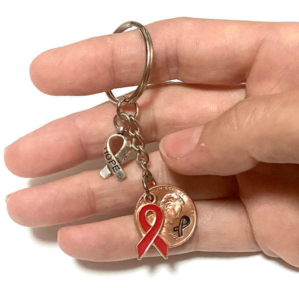 A red ribbon awareness charm on a 3" keychain with a silver HOPE charm attached to a Lincoln Cent with a detailed design of an awareness ribbon above the date to make a great Lucky Penny Keychain. The ribbon represents blood cancers and disorders.