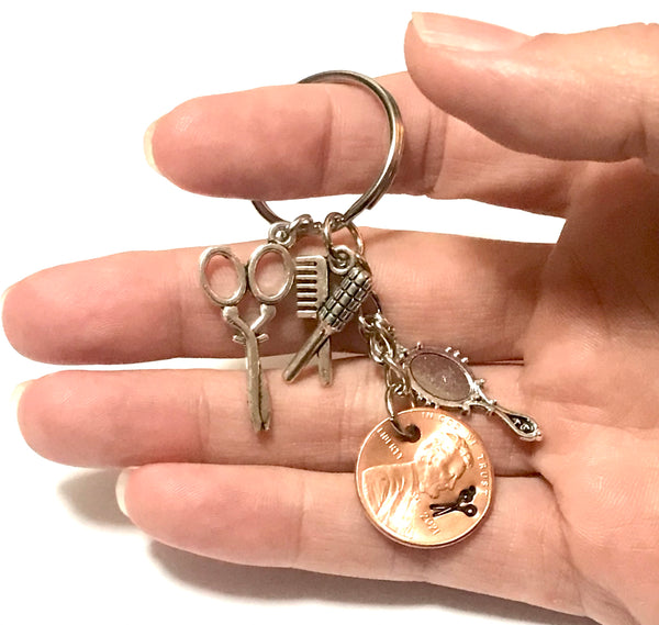 A Lucky Penny Keychain honoring Cosmetologists everywhere with a Silver set of Charms - Scissors, Hair Brush, and Mirror - including a Lincoln Cent with a pair of Scissors engraving.