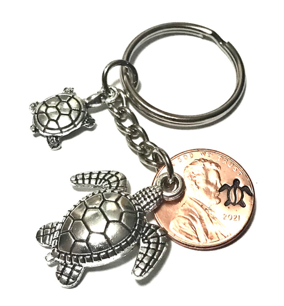 Two silver Sea Turtles-a mother and baby turtle-alongside a Lincoln Cent with an engraved Turtle above the date to make a Lucky Penny Keychain.