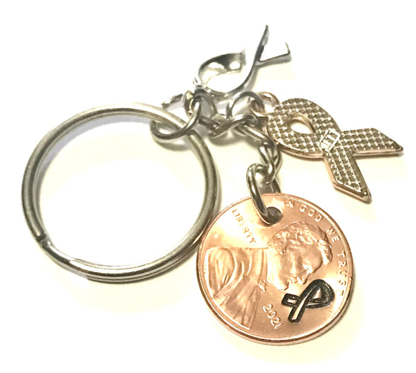 This Lung Cancer Awareness White Ribbon Charm Lucky Penny Keychain includes a Silver Ribbon engraved with the word "HOPE," and is paired with a Lincoln Cent that has a matching ribbon design above the date.