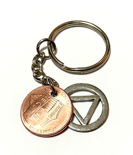 A Lucky Penny Keychain with a silver AA Alcoholics Anonymous Recovery Symbol attached to a Lincoln Cent engraved with the Sobriety symbol above the date.