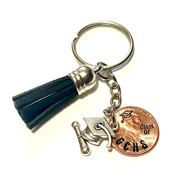 A black tassel charm with a silver grad cap and diploma charm attached to an engraved lucky penny.