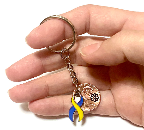 A Lucky Penny Keychain with a yellow and blue awareness ribbon charm attached to a penny with an engraving above the date.