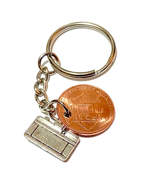 A photography inspired keychain with a silver camera charm attached to a Lincoln Cent with a camera design engraved above the date. It's an awesome Lucky Penny Keychain!