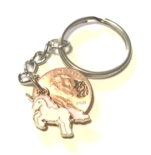 A Unicorn Lucky Penny Keychain with a Unicorn Charm with a Pink Mane and Tail with a hand stamped design above the date of a Lincoln Cent.
