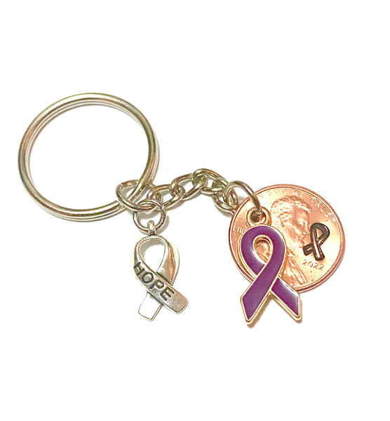 A purple awareness ribbon charm along with a silver HOPE charm attached to a Lincoln Cent with a detailed design of an awareness ribbon above the date for a great Lucky Penny Keychain.