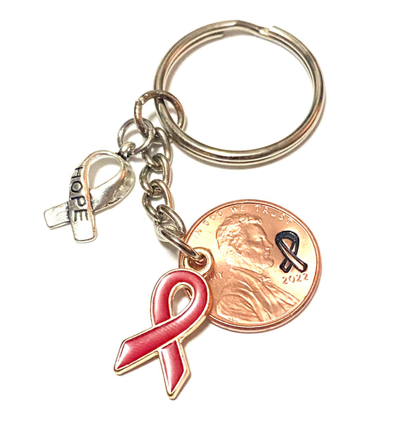 A red ribbon awareness charm on a 3" keychain with a silver HOPE charm attached to a Lincoln Cent with a detailed design of an awareness ribbon above the date to make a great Lucky Penny Keychain. The ribbon represents blood cancers and disorders.