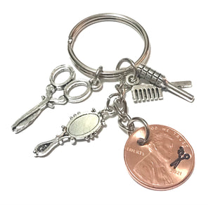 A Lucky Penny Keychain honoring Cosmetologists everywhere with a Silver set of Charms - Scissors, Hair Brush, and Mirror - including a Lincoln Cent with a pair of Scissors engraving.