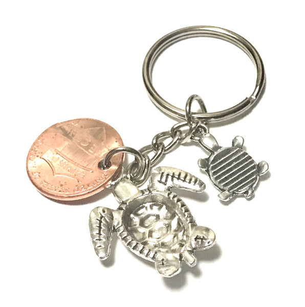 Two silver Sea Turtles-a mother and baby turtle-alongside a Lincoln Cent with an engraved Turtle above the date to make a Lucky Penny Keychain.