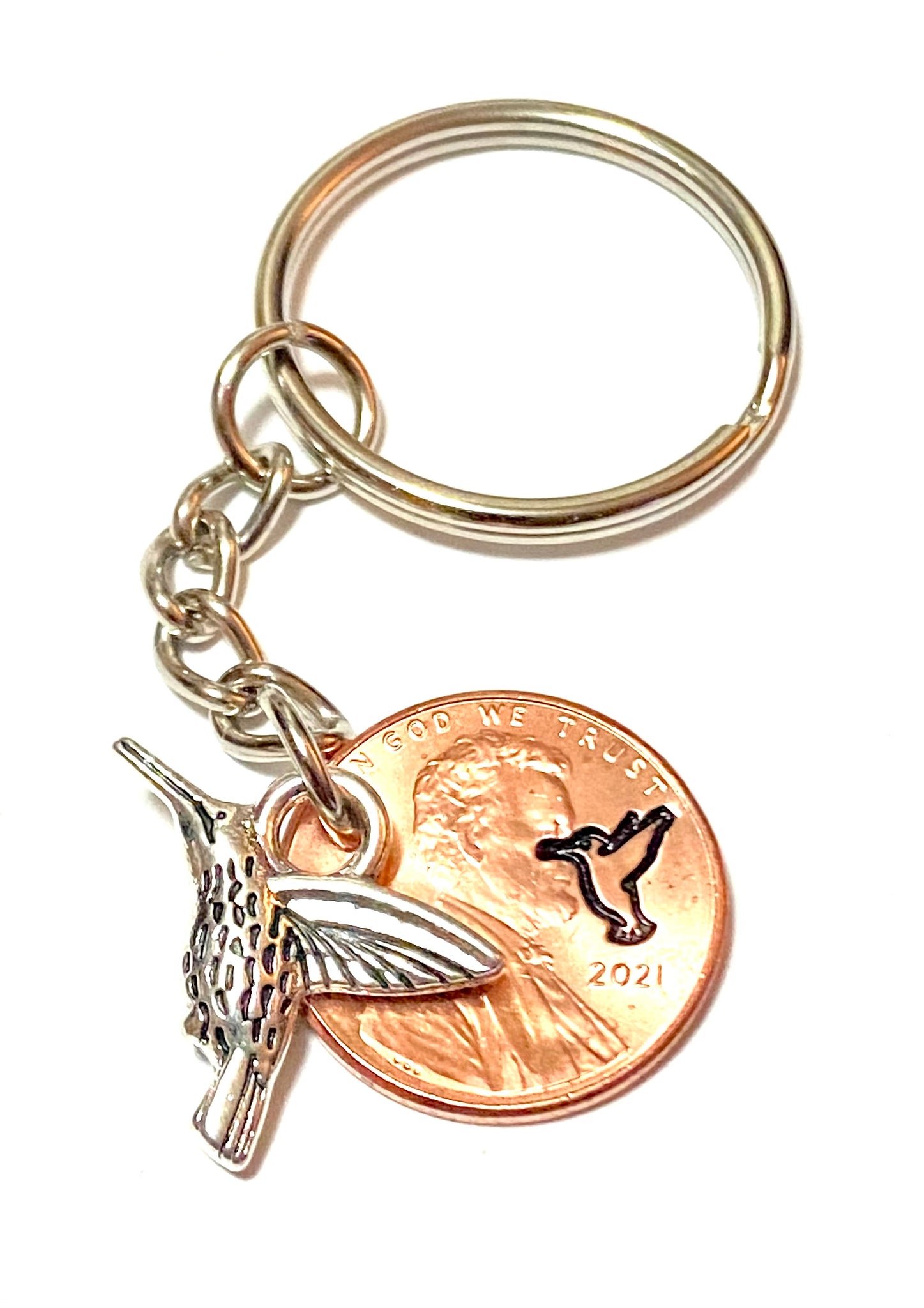 A Silver Hummingbird Charm attached to an engraved Lincoln Cent with a matching design above the date of a Lincoln Cent.