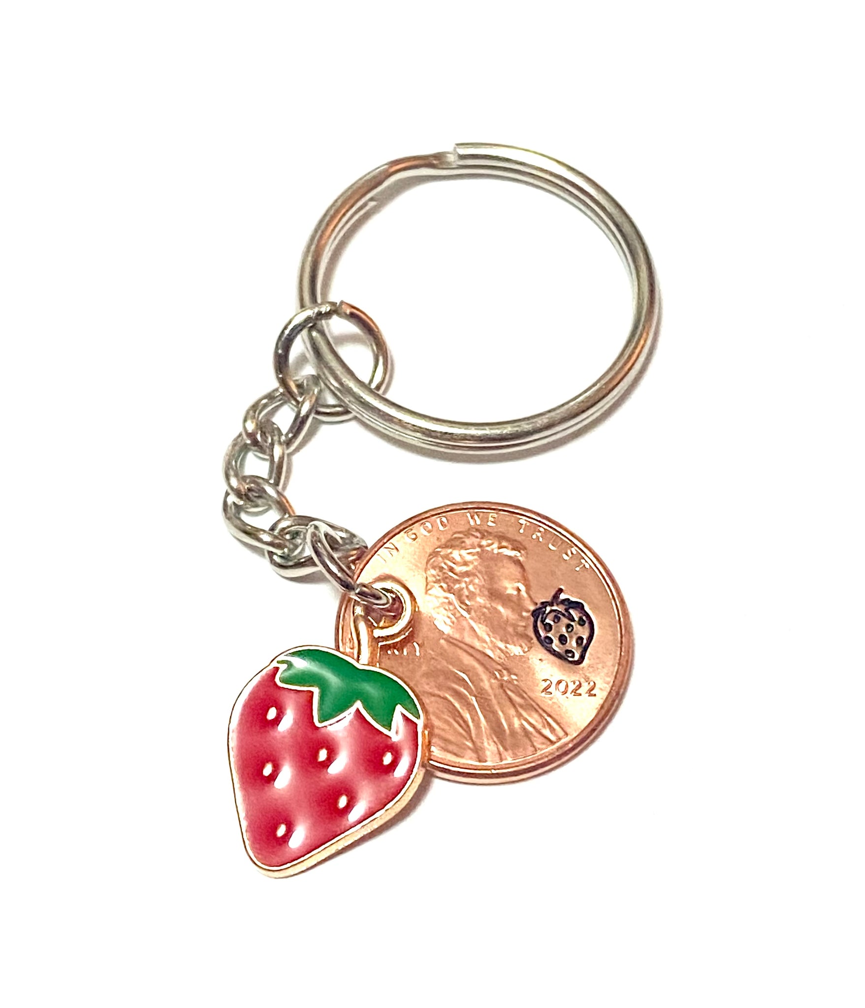 A red strawberry charm attached to a Lucky Penny Keychain with a detailed strawberry design engraved above the date of a Lincoln Cent.