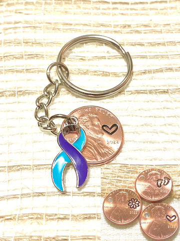A purple and teal ribbon charm to help raise awareness for Suicide Prevention that includes an engraving of a heart design above the date of a penny.