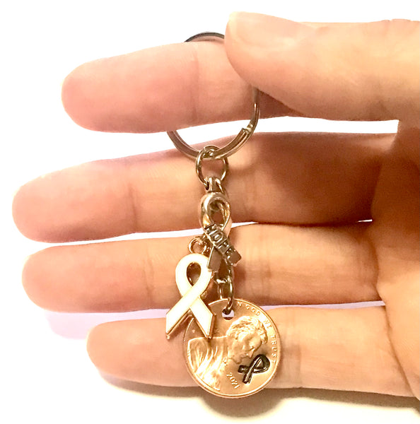 This Lung Cancer Awareness White Ribbon Charm Lucky Penny Keychain includes a Silver Ribbon engraved with the word "HOPE," and is paired with a Lincoln Cent that has a matching ribbon design above the date.